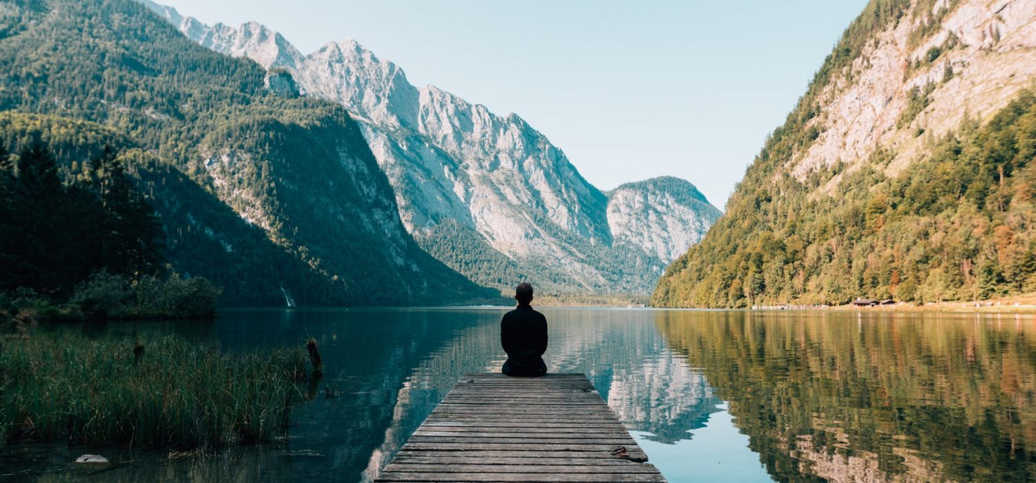 traveler sitting alone at the edge of a dock looking into nature