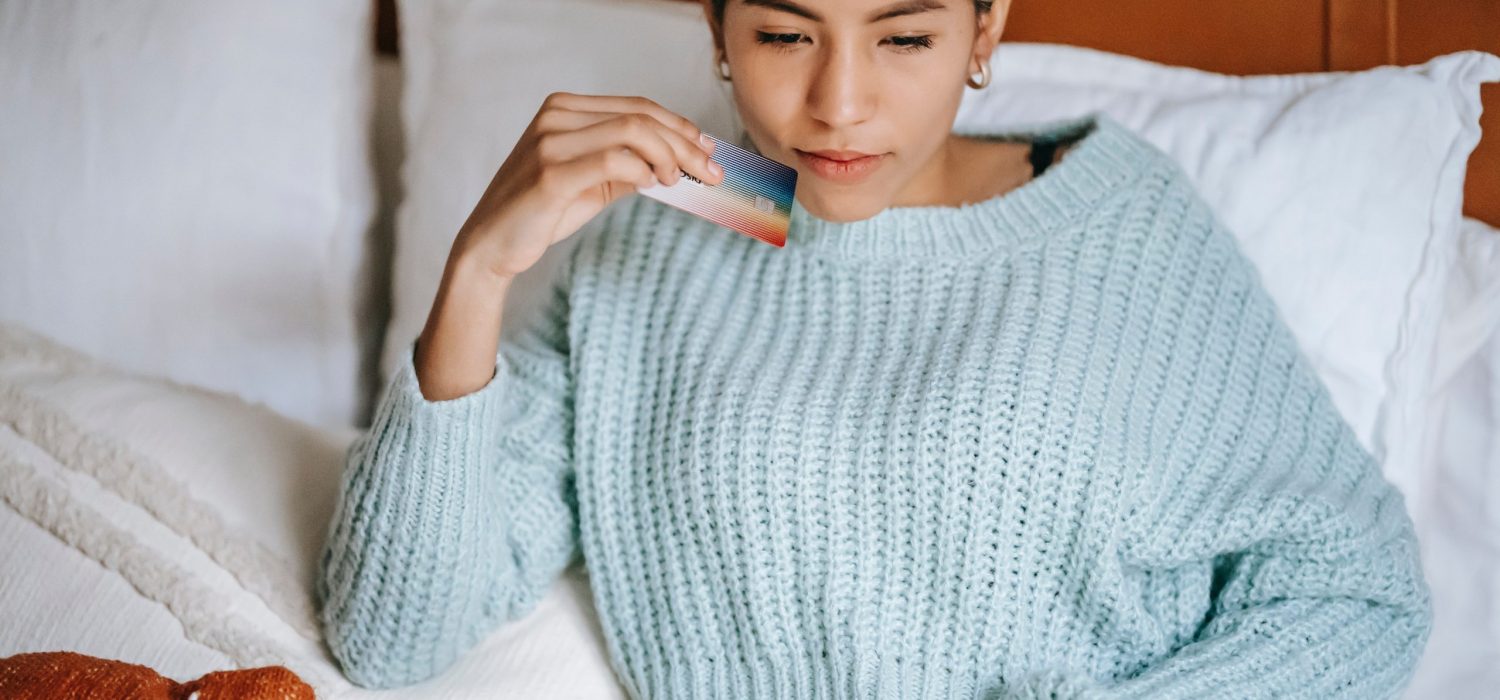 woman sitting on a bed holding a credit card while typing on a laptop